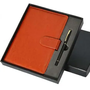Detailopname van het oranje notitieboek en de zwarte pen in een elegante geschenkdoos.