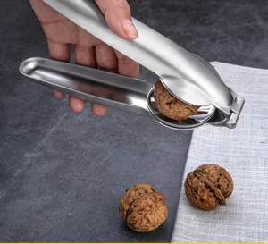 Stainless steel nutcracker detail view, showing the tool cracking a fresh walnut on table.