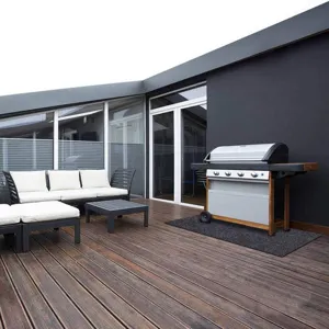 Detalle de la alfombrilla ignifuga para barbacoa exterior en terraza de madera segura.