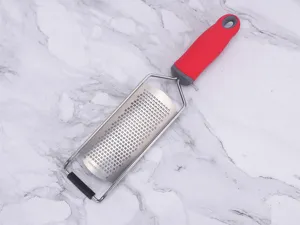 Stainless steel cheese grater detail showing sharp micro-blades and ergonomic red handle.