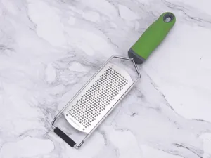 Detailed view of the stainless steel cheese and lemon grater with ergonomic green handle.