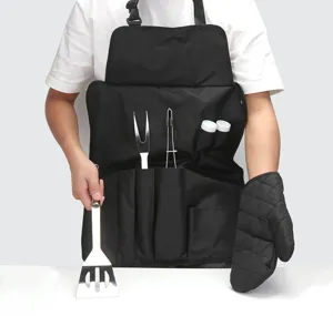 Detailed view of black BBQ apron tool set with stainless steel spatula, fork, and mitt.