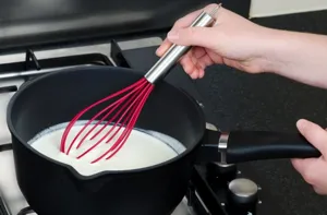 Detailansicht des roten Silikon Schneebesens mit Edelstahlgriff beim Rühren im Topf.