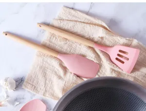 Silicone kitchen utensil detail showing pink spatula and slotted turner with natural wood handle.