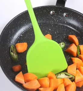 Primer plano detallado de una espátula de silicona verde brillante con verduras frescas.