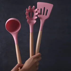 Juego de utensilios de cocina de silicona rosa con mangos de madera, espátula y cucharon incluidos.