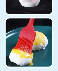 Detailed view of the red silicone oil basting brush applying sauce on food in kitchenware.