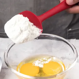 Red silicone spatula for kitchen baking holding flour over a glass bowl with fresh eggs