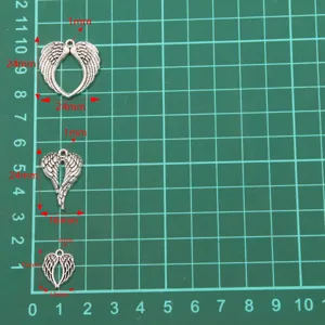 Close-up detail shot of DIY alloy hollow angel wing pendant charms with size grid.
