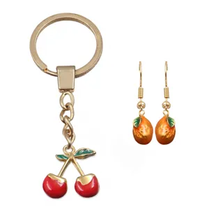 Emaillierter Kirsch-Schlüsselanhänger und orangefarbene Ohrringe mit farbenfrohem Frucht-Design.
