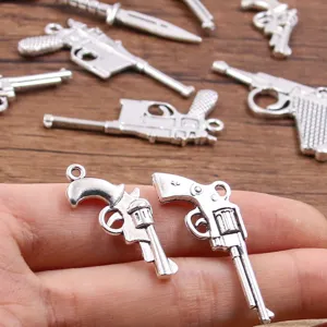 Close-up van miniatuur metalen wapenbedels, gedetailleerde pistool en dagger DIY sieraden hanger.