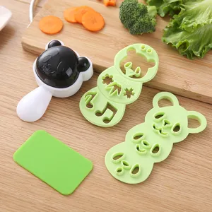 Detail view of cartoon animal rice mold and seaweed cutter set on wood board with fresh veggies.