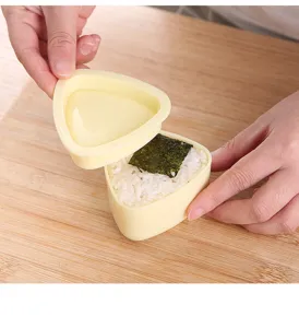 Detaillierte Nahaufnahme einer gelben Kunststoff Dreiecks Onigiri Form bei der Zubereitung.