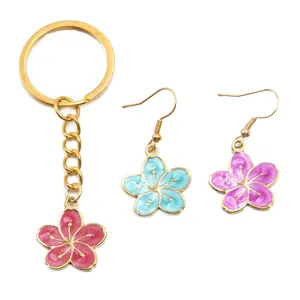 Vue détaillée d'un porte-clés fleur en émail coloré et de boucles d'oreilles assorties dorées.