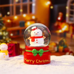 Close-up of a charming Christmas snow globe with cute snowman, red base and green bow for decor.