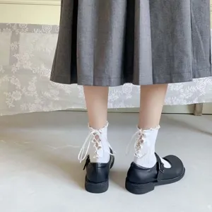 Detailansicht weißer Spitzen-Rüschen-Socken kombiniert mit schwarzen Schuhen und Rock.