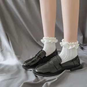 Detailansicht von weißen Spitzenrüschensocken kombiniert mit schwarzen Lackschuhen im süßen Stil.