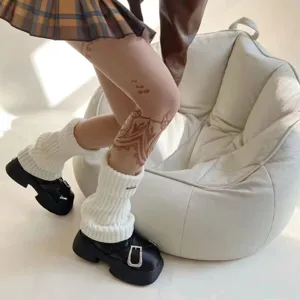 Detailed close-up of white knit leg warmers styled with black platform buckled shoes.