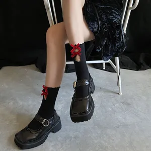 Close-up detail of cute black mid-calf socks with red bows, lace lettuce edge and hollow design.