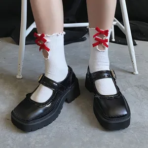 Close-up of white ribbed mid-calf socks with red flocked bows and lace-up details on shoes.