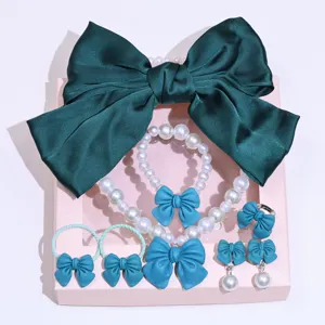 Detailed view of children jewelry set with green bow hair clip and pearl necklace.
