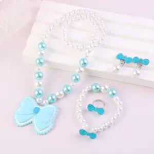 Close-up of children jewelry set featuring blue bow pendants and white pearls, detail view.