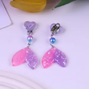 Close-up of cute children clip-on earrings with glitter pink purple mermaid tail pendants.