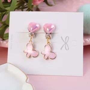 Close-up detail of cute pink heart and butterfly clip-on earrings on white display card.