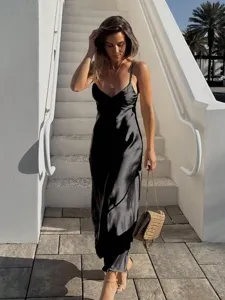 Détail de robe midi en satin noir, vêtement élégant style station balnéaire, scène en extérieur.