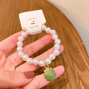 Detail view of a cute pearl beaded bracelet featuring a green shell pendant and white tag.