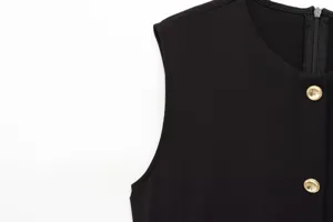 Detail shot of black sleeveless midi dress upper part, round neck, gold buttons, back zipper.