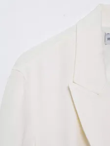 Gros plan détaillé du col et de la texture des épaules d'un blazer en lin blanc.