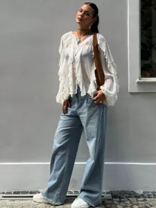 Detailed view of women's white ruffled V-neck long sleeve shirt worn in outdoor street style.