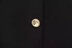 Close-up detail of black fabric with a stylish metallic gold textured button, premium clothing trim.
