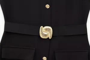 Detailed close-up product shot of black midi dress with gold metal buckle and buttons.