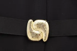 Close-up detail of women's black dress featuring elastic waistband and abstract gold metal buckle.