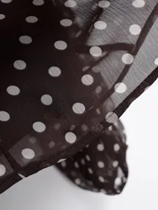 Close-up detail shot of a chic dark sheer polka dot long sleeve blouse fabric hem.