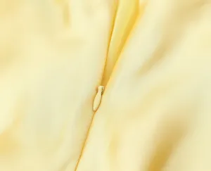 Gros plan sur la fermeture éclair d'une robe en satin jaune, tissu lisse et belle finition.