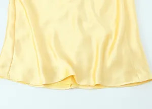 Vue détaillée de l'ourlet de robe en satin de soie jaune, texture lisse et élégante.