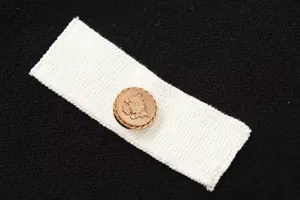 Detailansicht des eleganten goldenen Metallknopfs auf weißem Stoffmuster für schicke Strickwaren.