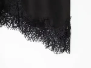 Black satin slip dress detail, delicate eyelash lace hem trim, elegant women's apparel close-up.