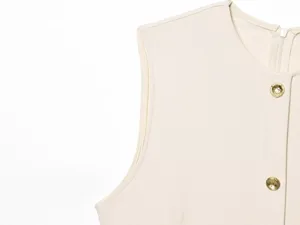Detailed close-up view of the elegant beige sleeveless dress with round neck and gold buttons.