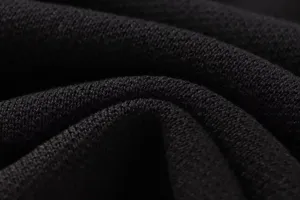 Schwarzes Strickgewebe Detail Nahaufnahme zeigt feine Textur und weiche Materialfalten.