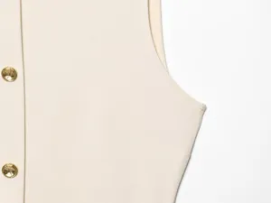Beige sleeveless dress detail closeup, showing elegant gold buttons and fine tailoring.