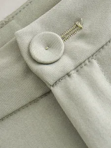 Gros plan sur la ceinture, le bouton et le tissu sergé fin du pantalon décontracté pour femme.