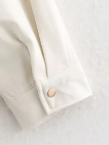 Detailed view of off-white long sleeve cuff with golden metallic button on soft texture.