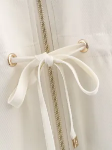 Close-up detail of women's white top featuring metal zipper, eyelets and elegant drawstring bow.