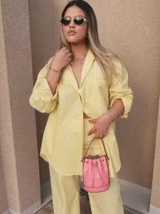 Detail view of a casual yellow striped oversized shirt and pants set worn by model outdoors.