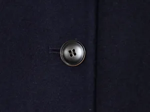 Close-up detail of dark blue woolen coat fabric texture featuring a classic four-hole button.
