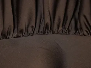 Brown satin dress fabric detail, smooth texture, pleated seam close-up, elegant fabric.